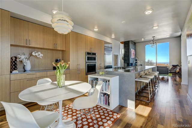 kitchen with hardwood / wood-style flooring, a kitchen breakfast bar, a kitchen island with sink, and hanging light fixtures