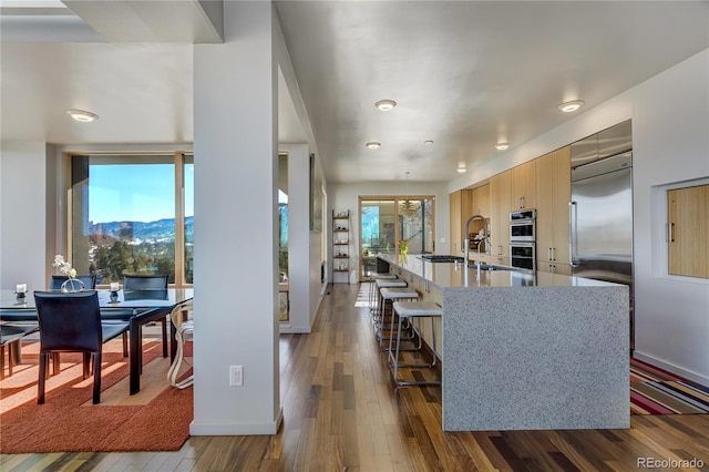 kitchen with light brown cabinetry, a breakfast bar area, a center island with sink, dark hardwood / wood-style floors, and stainless steel appliances