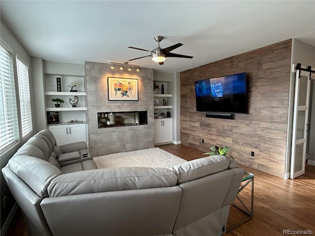 living room featuring ceiling fan, built in features, hardwood / wood-style floors, wooden walls, and a fireplace