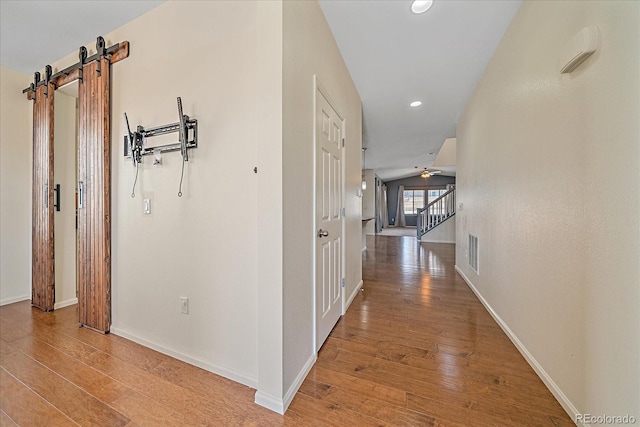 hallway featuring vaulted ceiling, a barn door, and light hardwood / wood-style floors