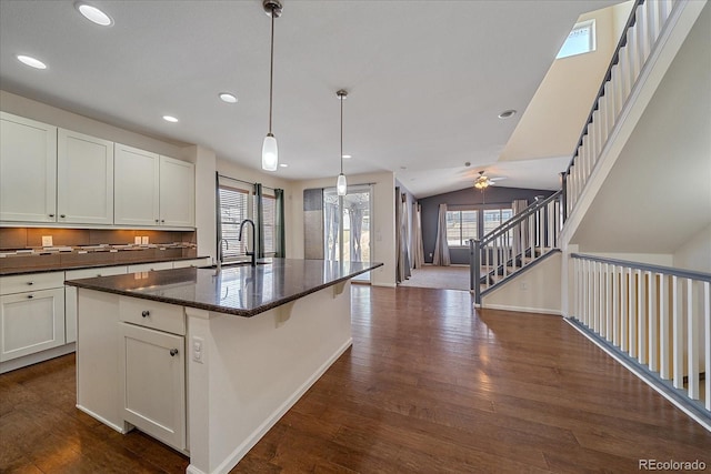 kitchen with sink, white cabinetry, hanging light fixtures, dark stone countertops, and a kitchen island with sink