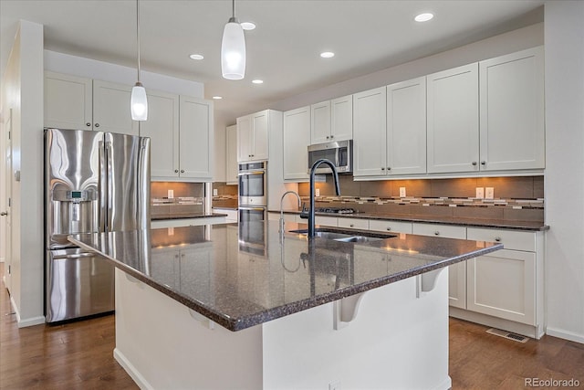 kitchen featuring white cabinetry, appliances with stainless steel finishes, an island with sink, and hanging light fixtures