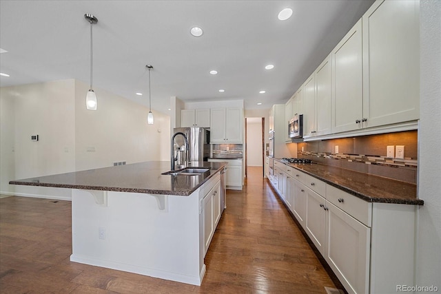 kitchen featuring appliances with stainless steel finishes, white cabinetry, a center island with sink, a kitchen bar, and decorative light fixtures