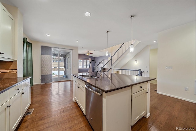 kitchen featuring sink, dark stone countertops, hanging light fixtures, a center island with sink, and stainless steel dishwasher