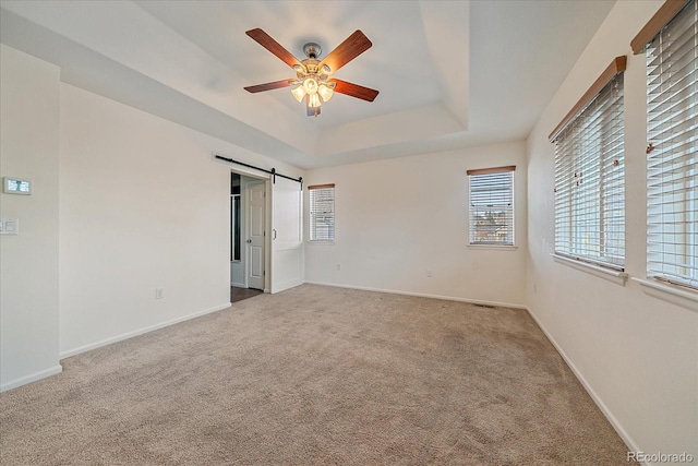 unfurnished bedroom with a raised ceiling, a barn door, carpet, and ceiling fan