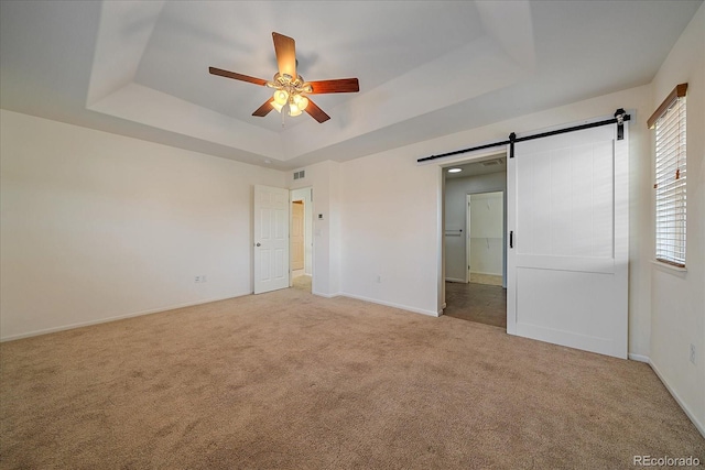 unfurnished bedroom featuring light carpet, a raised ceiling, ceiling fan, and a barn door