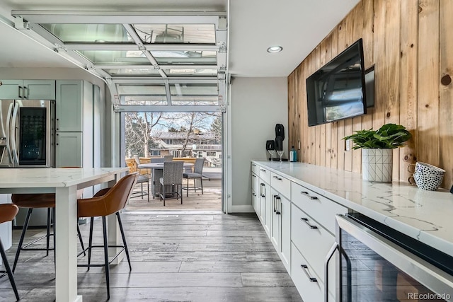 kitchen featuring green cabinets, white cabinets, light stone countertops, beverage cooler, and stainless steel fridge