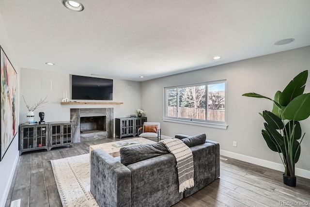 living room with a textured ceiling, recessed lighting, a premium fireplace, baseboards, and hardwood / wood-style floors