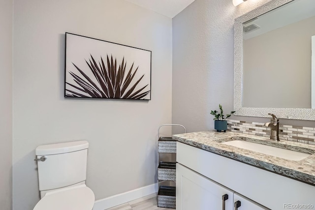 half bath with tasteful backsplash, visible vents, toilet, vanity, and wood finished floors