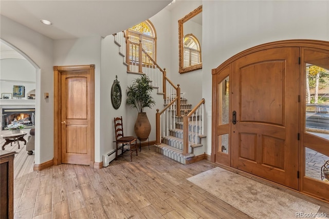 entrance foyer featuring arched walkways, light wood finished floors, a lit fireplace, baseboards, and stairs