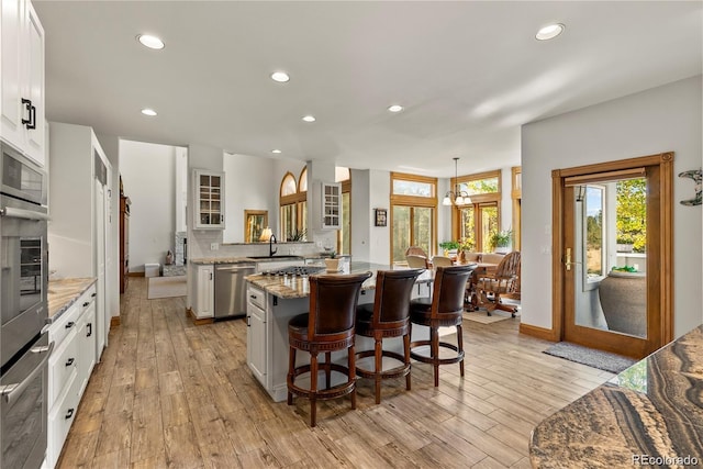 kitchen with light wood-style flooring, decorative backsplash, appliances with stainless steel finishes, glass insert cabinets, and a kitchen breakfast bar