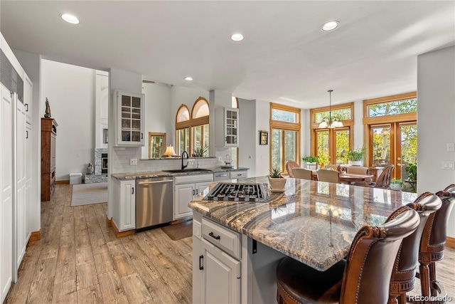 kitchen with light wood finished floors, tasteful backsplash, appliances with stainless steel finishes, a sink, and a kitchen bar