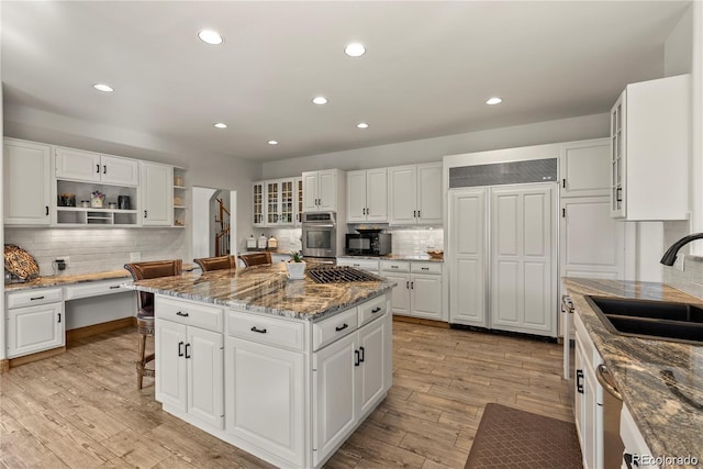 kitchen with built in study area, a center island, light wood-style floors, open shelves, and a sink