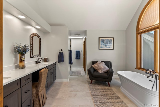 bathroom featuring a freestanding bath, double vanity, a sink, and baseboards