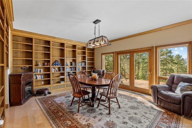 dining area with a glass covered fireplace, crown molding, and light wood-style flooring