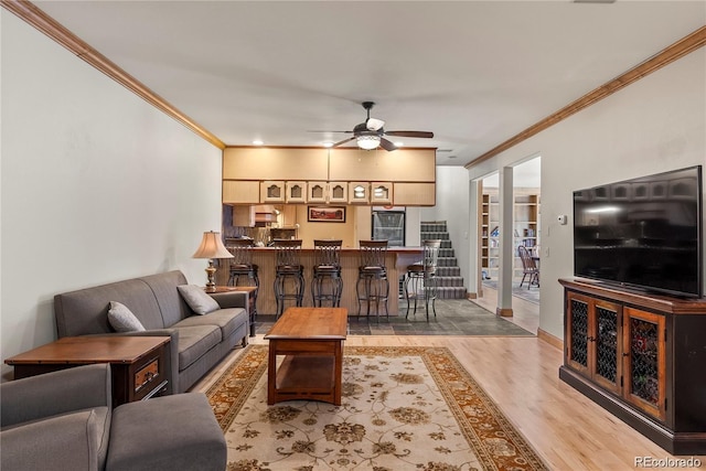 living room featuring indoor bar, light wood-style floors, ornamental molding, ceiling fan, and baseboards