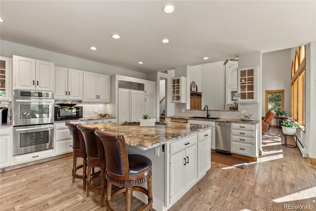 kitchen with a center island, appliances with stainless steel finishes, a baseboard heating unit, glass insert cabinets, and a sink