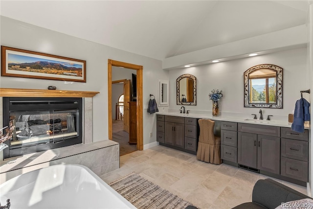 full bathroom featuring a freestanding bath, a multi sided fireplace, vaulted ceiling, vanity, and baseboards