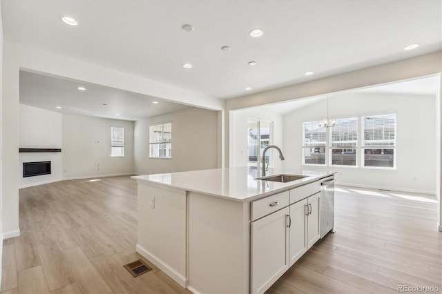 kitchen with sink, white cabinetry, light wood-type flooring, stainless steel dishwasher, and an island with sink