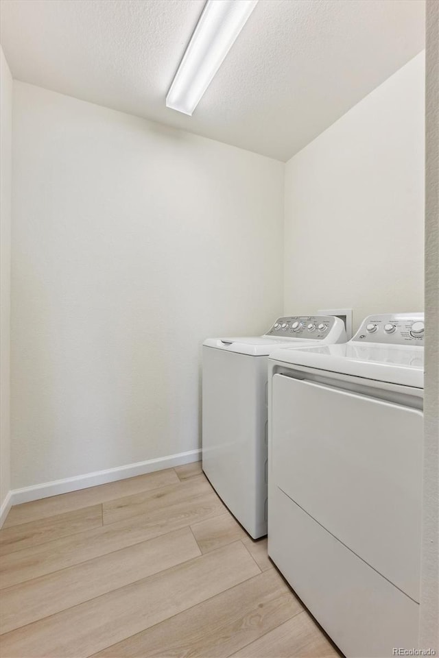 laundry room with washing machine and dryer, a textured ceiling, and light wood-type flooring