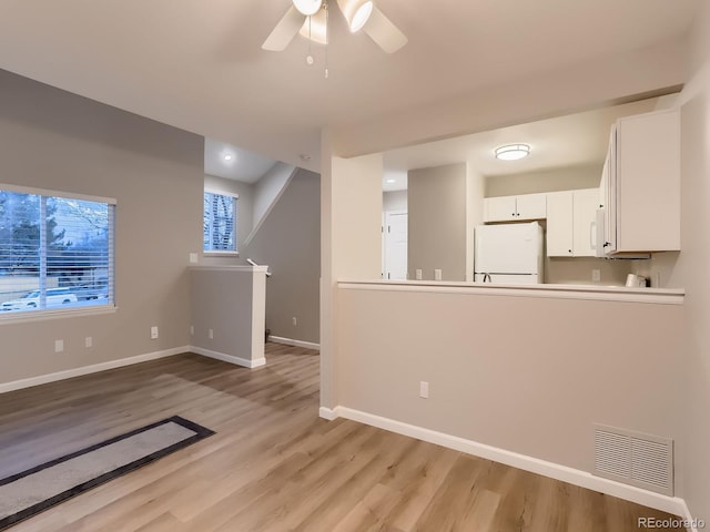 unfurnished living room with light wood-style floors, visible vents, ceiling fan, and baseboards