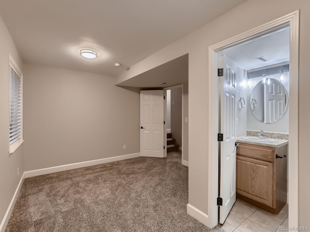 unfurnished bedroom with light tile patterned floors, light colored carpet, visible vents, a sink, and baseboards