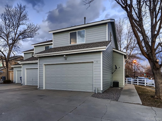 exterior space with roof with shingles, concrete driveway, central AC unit, fence, and a garage