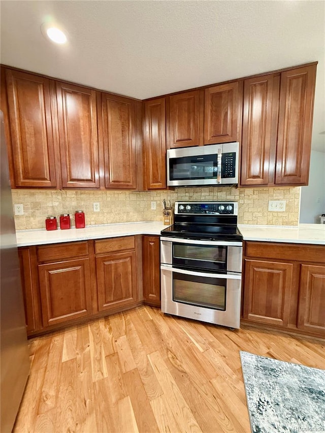 16063 E 106th Ct, Commerce City, CO 80022 - kitchen with appliances with stainless steel finishes, brown cabinetry, light wood-style floors, and tasteful backsplash