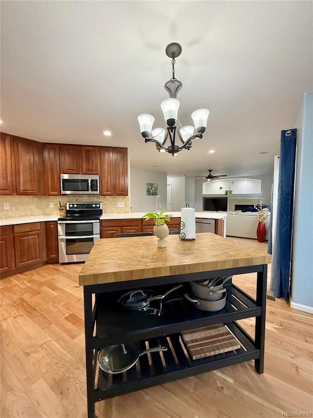 16063 E 106th Ct, Commerce City, CO 80022 - kitchen featuring stainless steel appliances, a chandelier, brown cabinetry, light wood-type flooring, and decorative backsplash