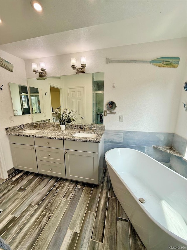 16063 E 106th Ct, Commerce City, CO 80022 - bathroom with a freestanding bath, a stall shower, double vanity, wood finished floors, and tile walls