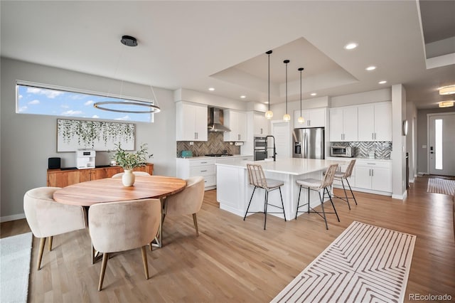 dining area featuring a tray ceiling, sink, a chandelier, and light wood-type flooring