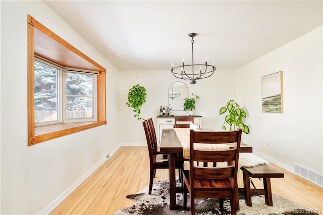 dining area featuring a notable chandelier, baseboards, visible vents, and light wood-style floors