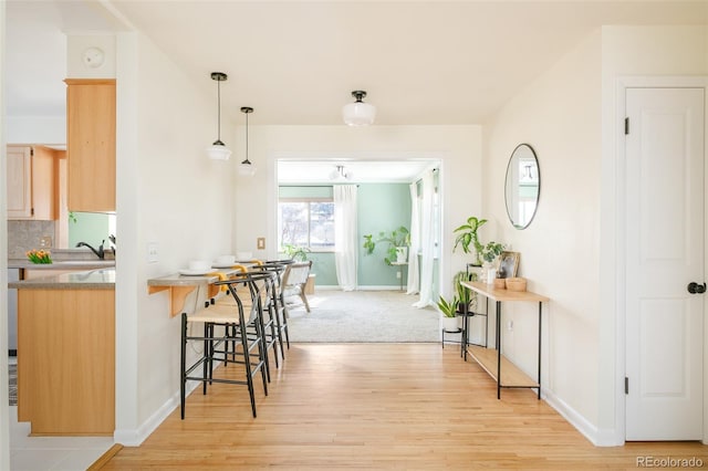 kitchen featuring light brown cabinets, hanging light fixtures, light wood-type flooring, decorative backsplash, and a kitchen bar