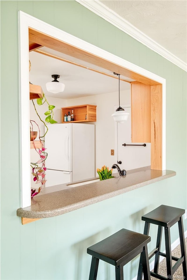 kitchen featuring decorative light fixtures, a breakfast bar area, freestanding refrigerator, and crown molding