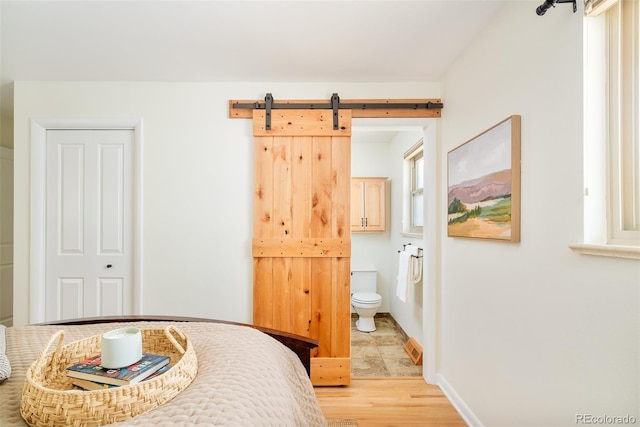 bedroom with light wood finished floors, ensuite bath, and baseboards