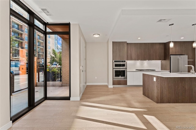 kitchen featuring appliances with stainless steel finishes, light hardwood / wood-style flooring, hanging light fixtures, white cabinets, and expansive windows