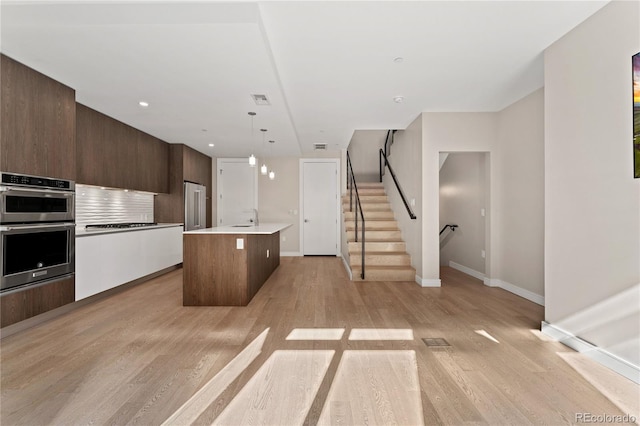 kitchen with light hardwood / wood-style floors, hanging light fixtures, stainless steel appliances, and a center island