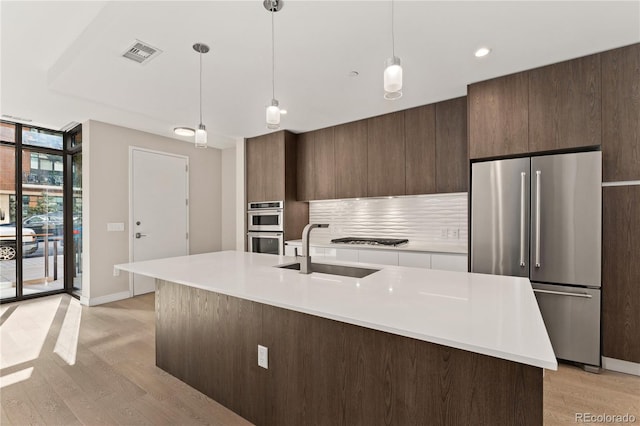 kitchen with a kitchen island with sink, decorative light fixtures, sink, a wall of windows, and appliances with stainless steel finishes