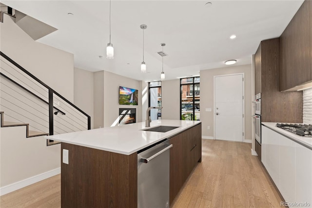 kitchen with a center island with sink, sink, light wood-type flooring, pendant lighting, and stainless steel appliances