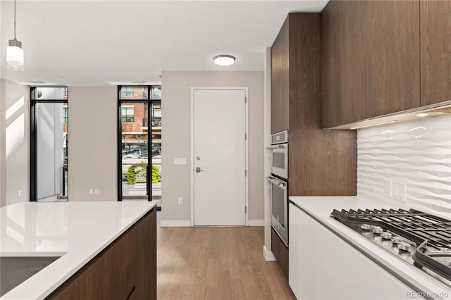 kitchen featuring hanging light fixtures, dark brown cabinetry, stainless steel gas cooktop, decorative backsplash, and light wood-type flooring