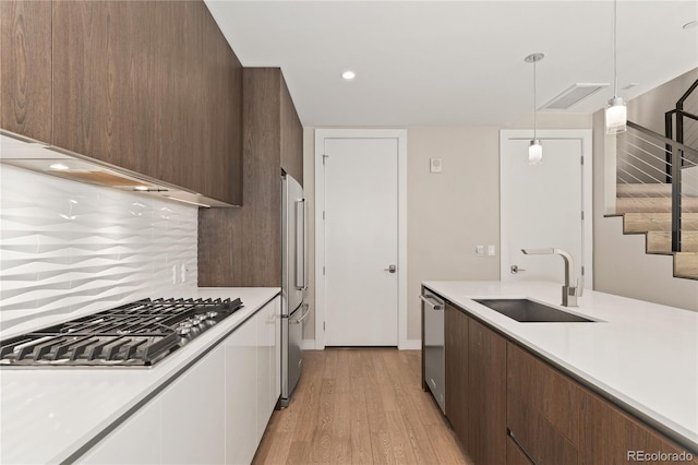 kitchen featuring appliances with stainless steel finishes, sink, light wood-type flooring, pendant lighting, and tasteful backsplash