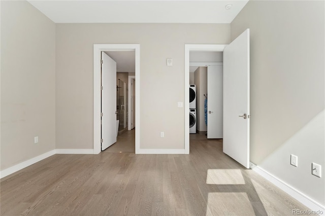 unfurnished bedroom with light hardwood / wood-style flooring and stacked washer and dryer