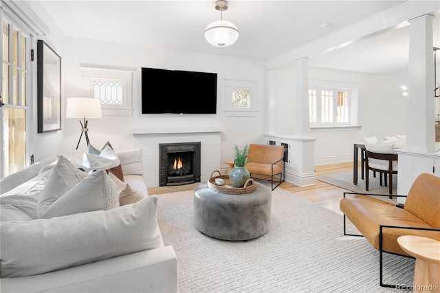 living room with light wood-type flooring, a brick fireplace, decorative columns, and baseboards