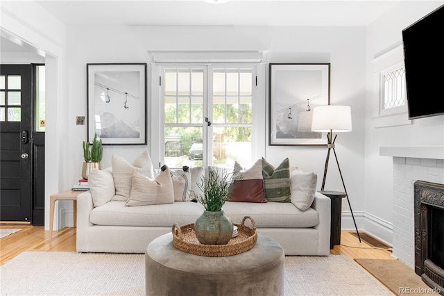 living area with a brick fireplace, visible vents, baseboards, and wood finished floors