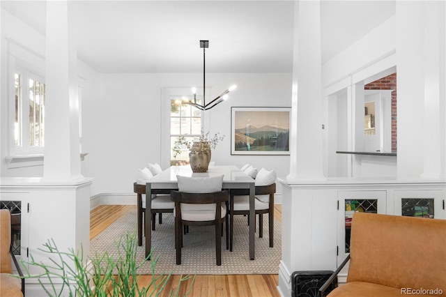 dining space with a chandelier, light wood-type flooring, and ornate columns