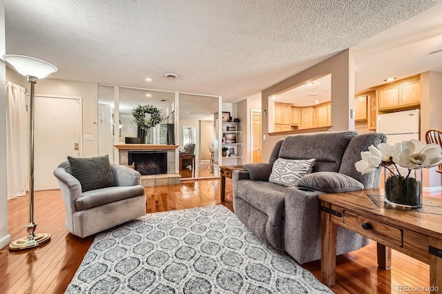 living area with visible vents, wood-type flooring, a textured ceiling, and a tile fireplace