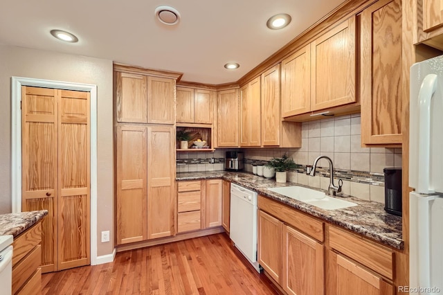 kitchen with a sink, dark stone countertops, backsplash, white appliances, and light wood finished floors