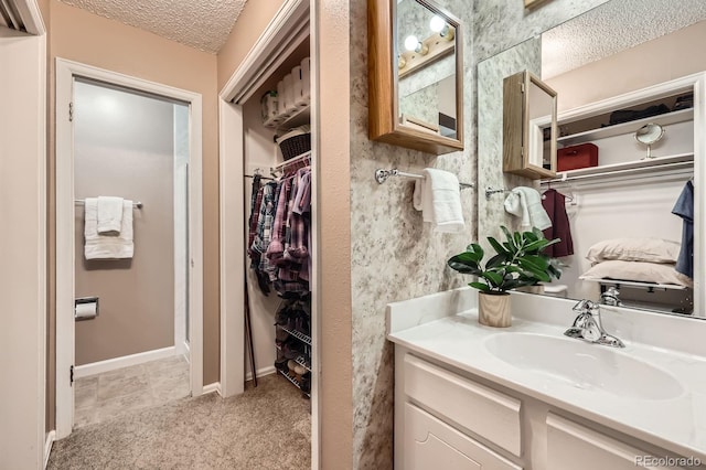 bathroom with vanity, a textured ceiling, a walk in closet, and baseboards