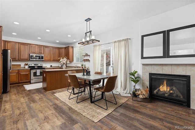 kitchen with hanging light fixtures, stainless steel appliances, dark wood-type flooring, a tiled fireplace, and a kitchen island