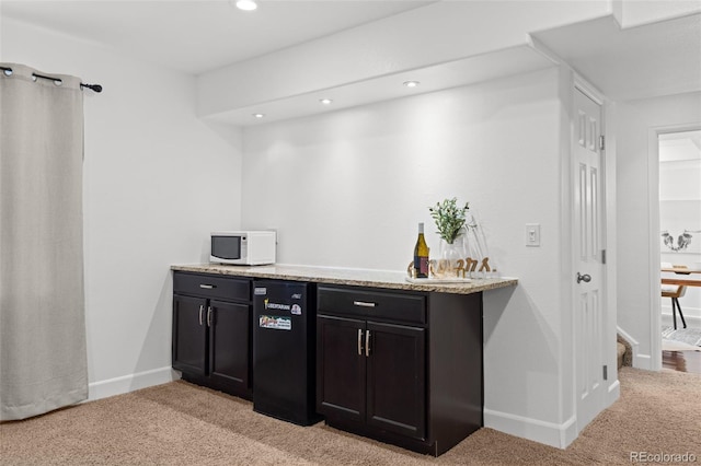 bar featuring light colored carpet, light stone counters, and fridge